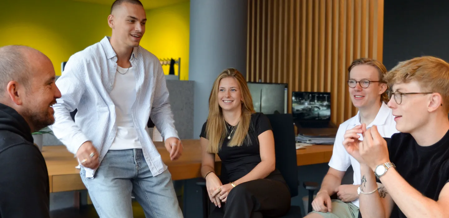 Fünf junge Menschen in einem modernen Büro, drei Männer und zwei Frauen, unterhalten sich und lächeln.