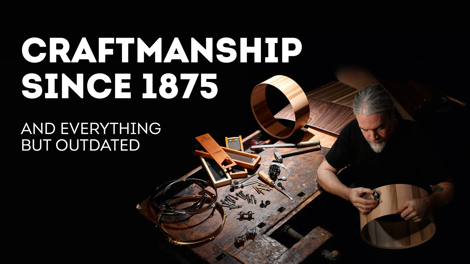 Älterer Mann an einer dramatisch ausgeleuchteten Werkbank hält eine Befestigung an eine Holztrommel, dazu werberische Headline "Craftmanship since 1875"